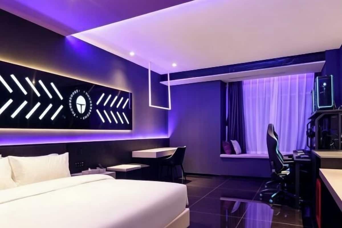 Ein modernes Hotelzimmer mit einem Bett, einem Schreibtisch, einem Sessel und einem am Wand montierten Fernseher.