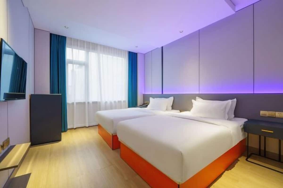 Ein Hotelzimmer mit zwei Betten, einem Flachbildfernseher, einem Schreibtisch und einem Fenster mit Vorhängen.