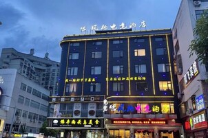 Un hotel de varios pisos con letreros iluminados, múltiples ventanas y diversos comercios en la planta baja.