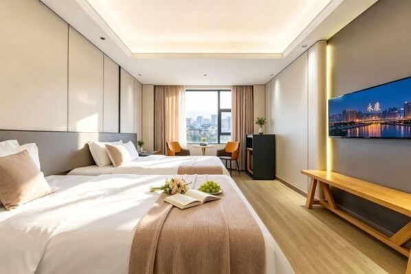 Ein Hotelzimmer mit zwei Betten, einem Schreibtisch, einem Sessel, einem Fernseher und Blick auf die Stadt.