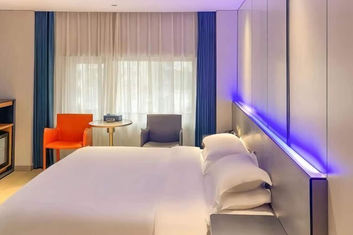 Ein Hotelzimmer mit einem großen Bett, zwei Stühlen, einem kleinen Tisch und einem Fernseher.