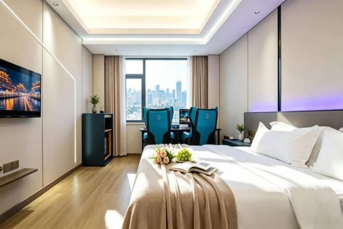 Ein Hotelzimmer mit Bett, Schreibtisch mit zwei Stühlen, Fernseher und Blick auf die Stadt.