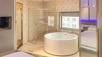 A modern bathroom with a large bathtub, a walk-in shower, and a bed with a view of the city.