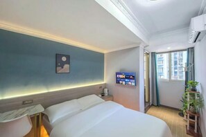 A hotel room with a bed, bedside table, wall-mounted TV, and a window with curtains.