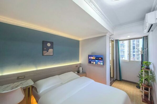 A hotel room with a bed, bedside table, wall-mounted TV, and a window with curtains.