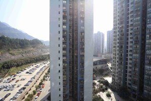 A high-rise building with multiple floors, a parking lot with several cars, and a mountainous landscape in the background.