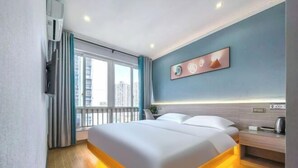 A modern hotel room with a large bed, a bedside table, a wall-mounted air conditioner, and a window with curtains. - Qiangxing Inn (Chongqing)