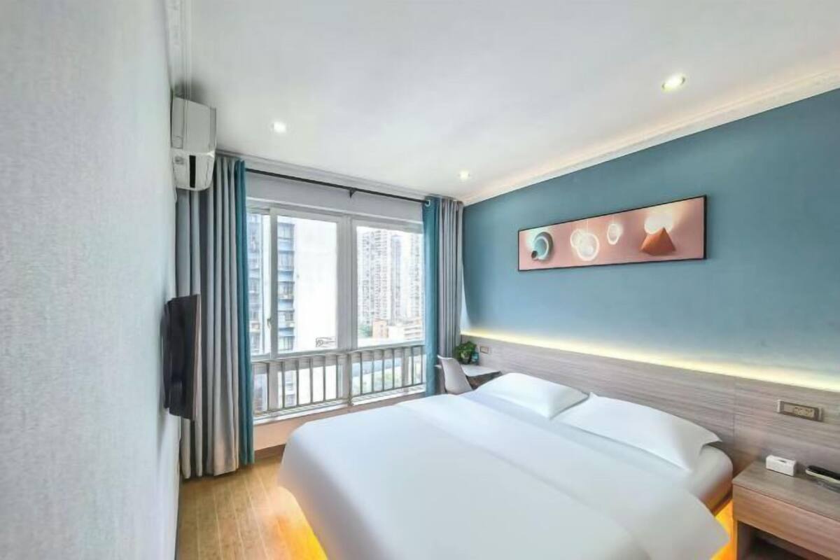 Habitación de hotel con cama, televisión, ventana con cortinas y una obra de arte en la pared.