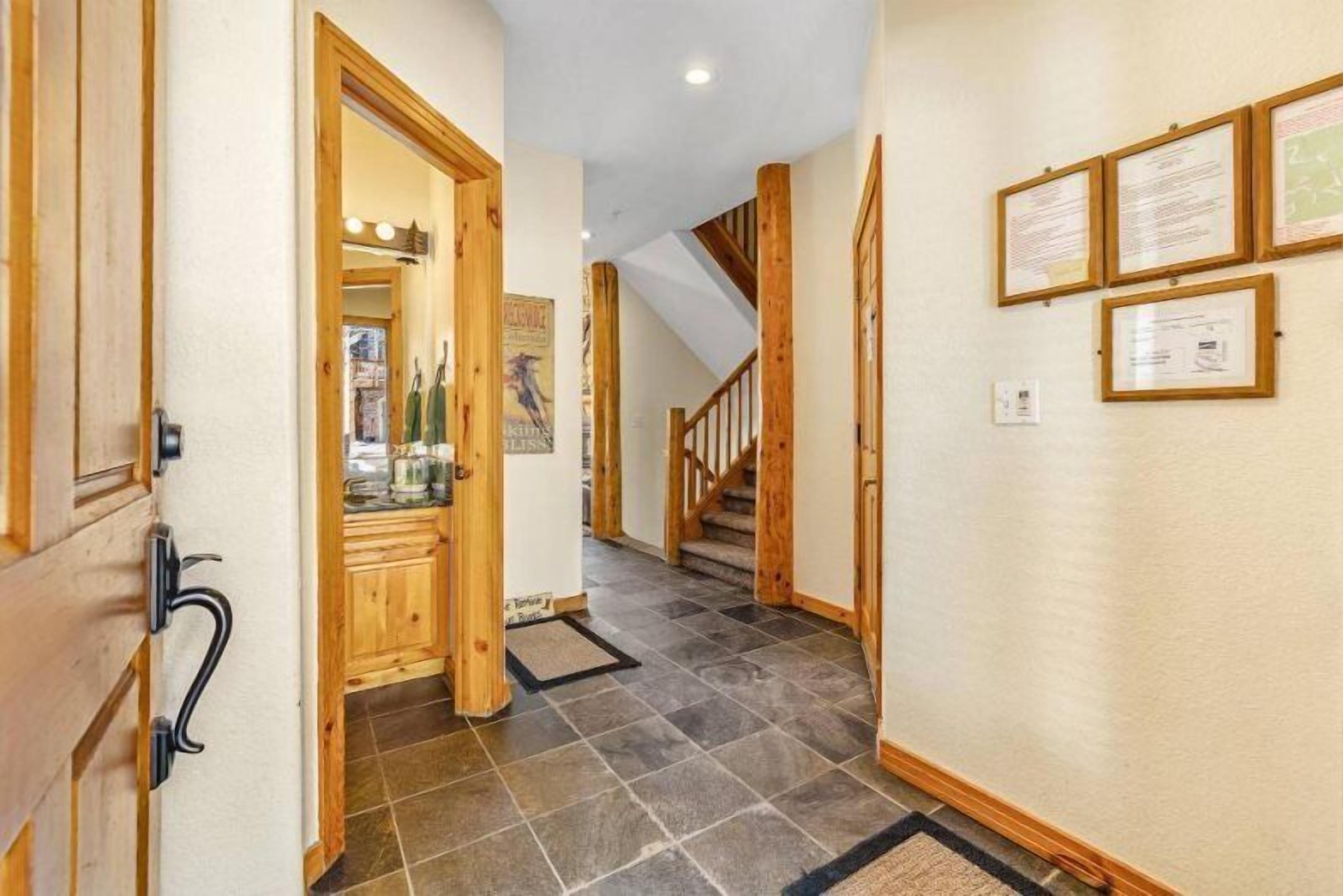 A hallway with wooden doors, a staircase, and framed certificates on the wall.