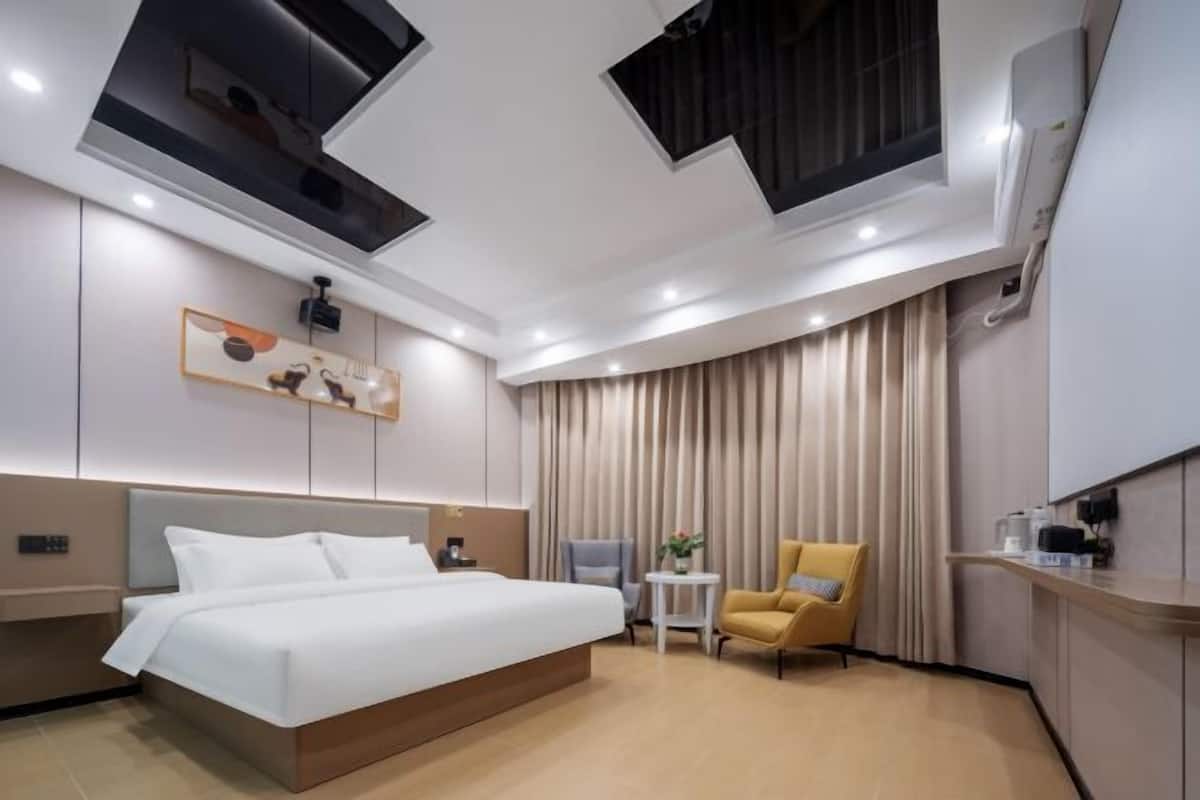 A modern hotel room with a large bed, a small table, a chair, and a window with curtains.