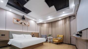 Una habitación de hotel moderna con una cama grande, una mesita, una silla y un ventanal con cortinas.