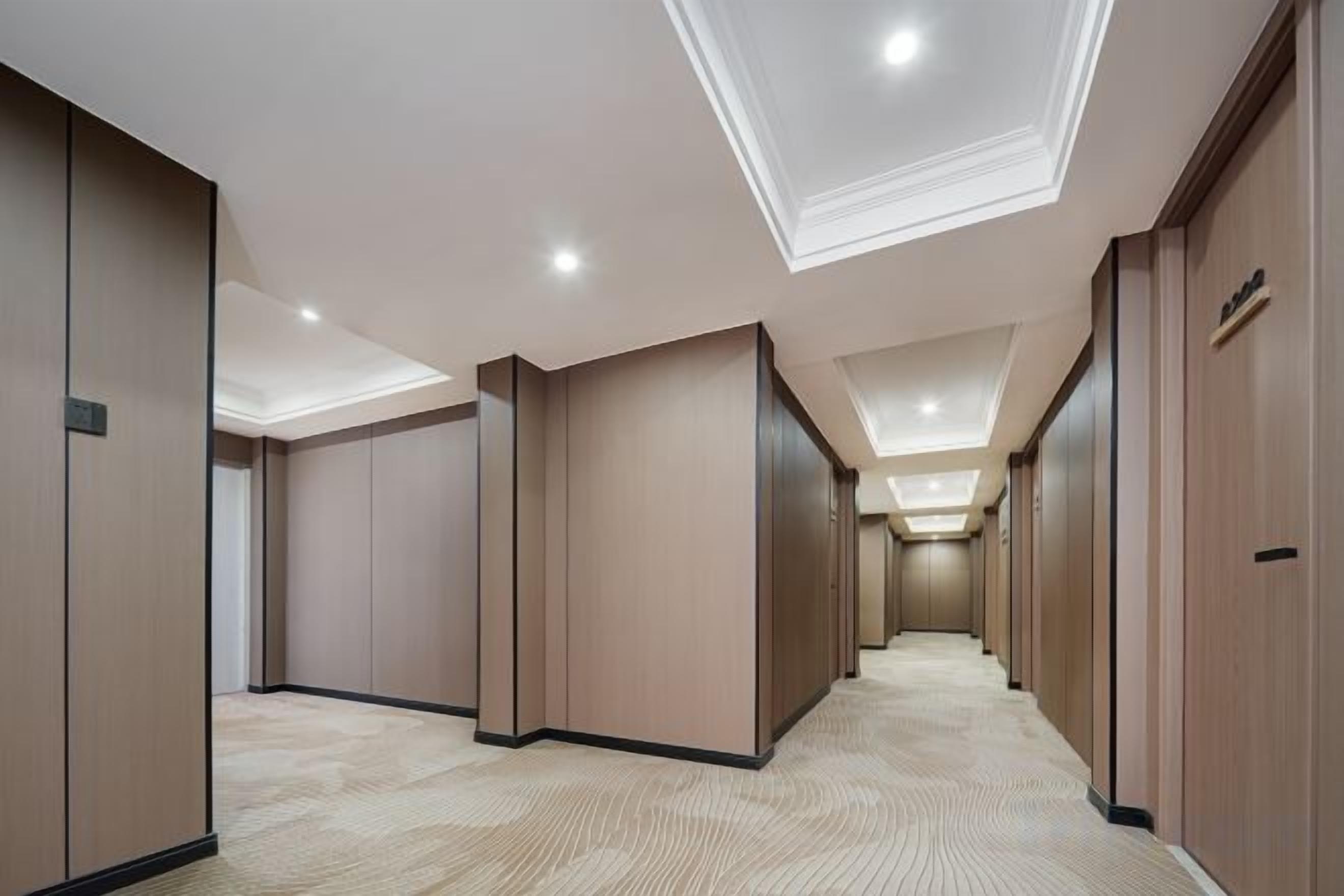 A hotel corridor with wooden panel walls, recessed ceiling lights, and a carpeted floor.