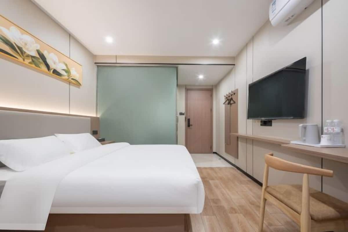 A modern hotel room with a bed, a desk, a TV, and a painting on the wall.