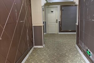 Un pasillo estrecho con alfombra estampada, una puerta blanca y una pared con azulejos.