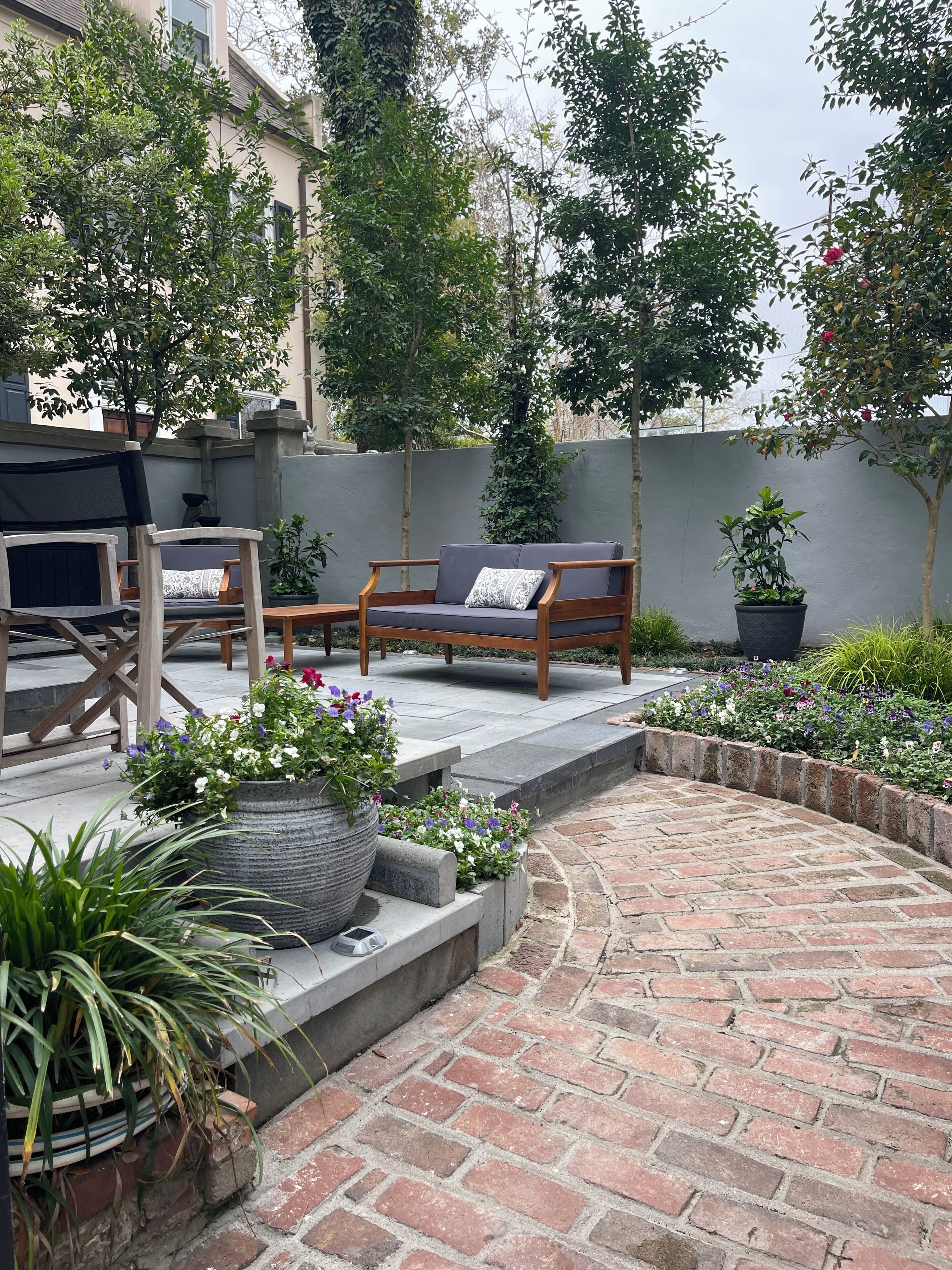 Un patio con muebles de exterior, un camino de ladrillo y plantas en macetas.