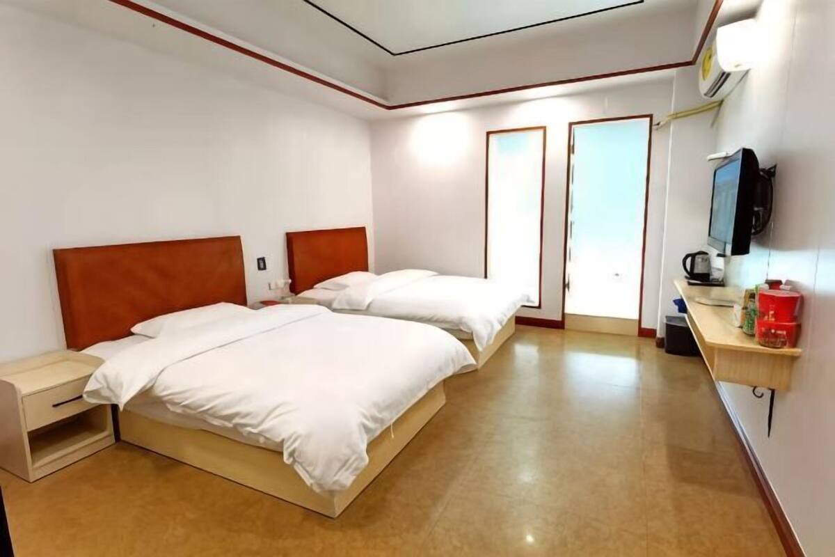 A hotel room with two beds, a bedside table, a TV, and a small shelf with items.