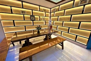 A dining area with a wooden table and bench, a wall with illuminated panels, and a tiled floor. - Wanli Hotel (Qinzhou)