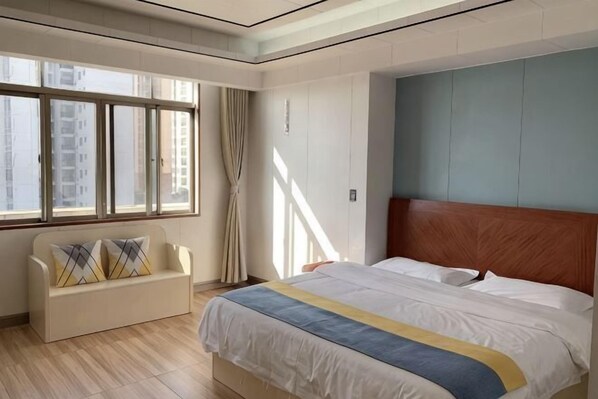 A hotel room with a bed, a sofa, a window with curtains, and a view of buildings. - Wanli Hotel (Qinzhou)