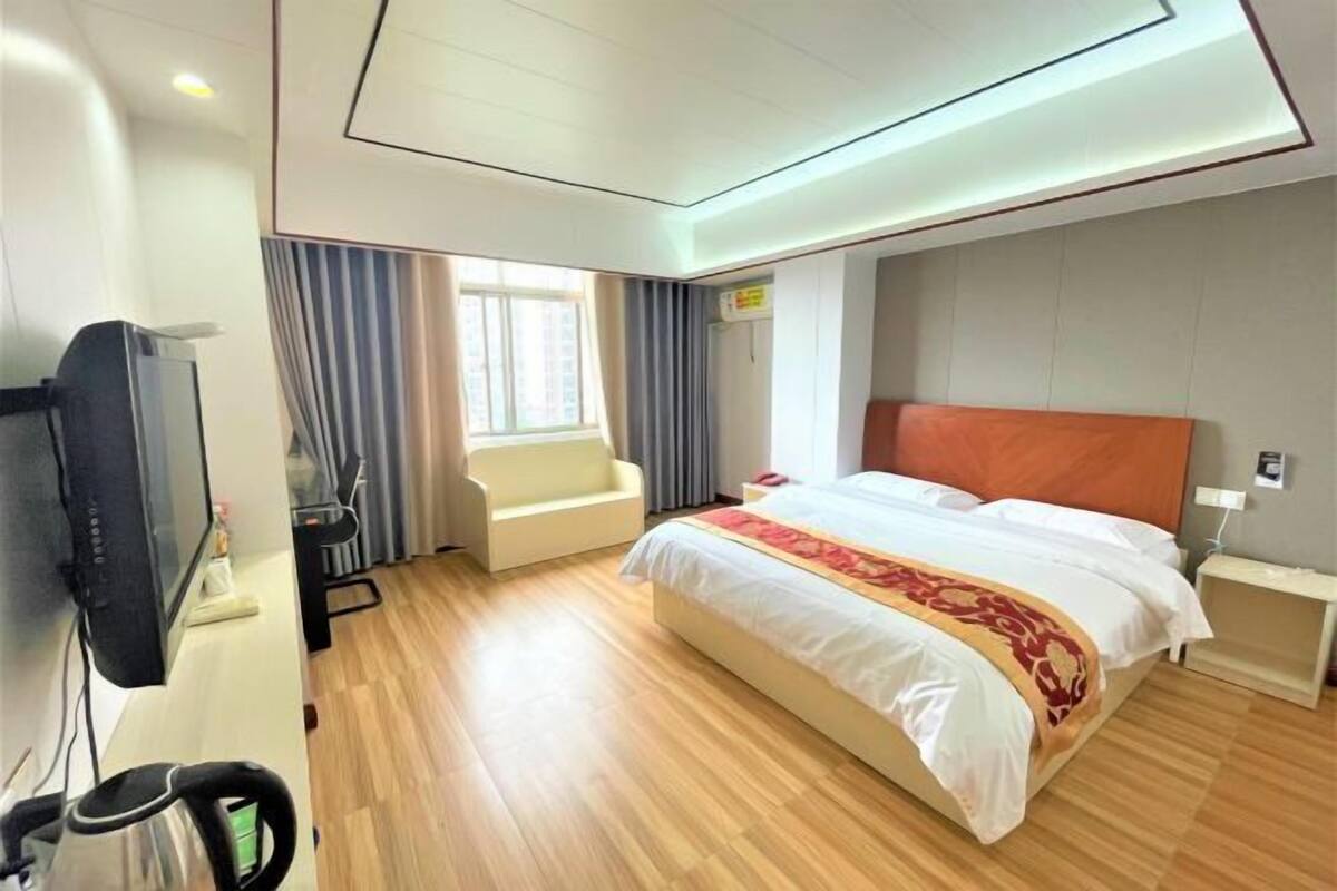 A hotel room with a large bed, a desk with a computer, a chair, and a window with curtains.