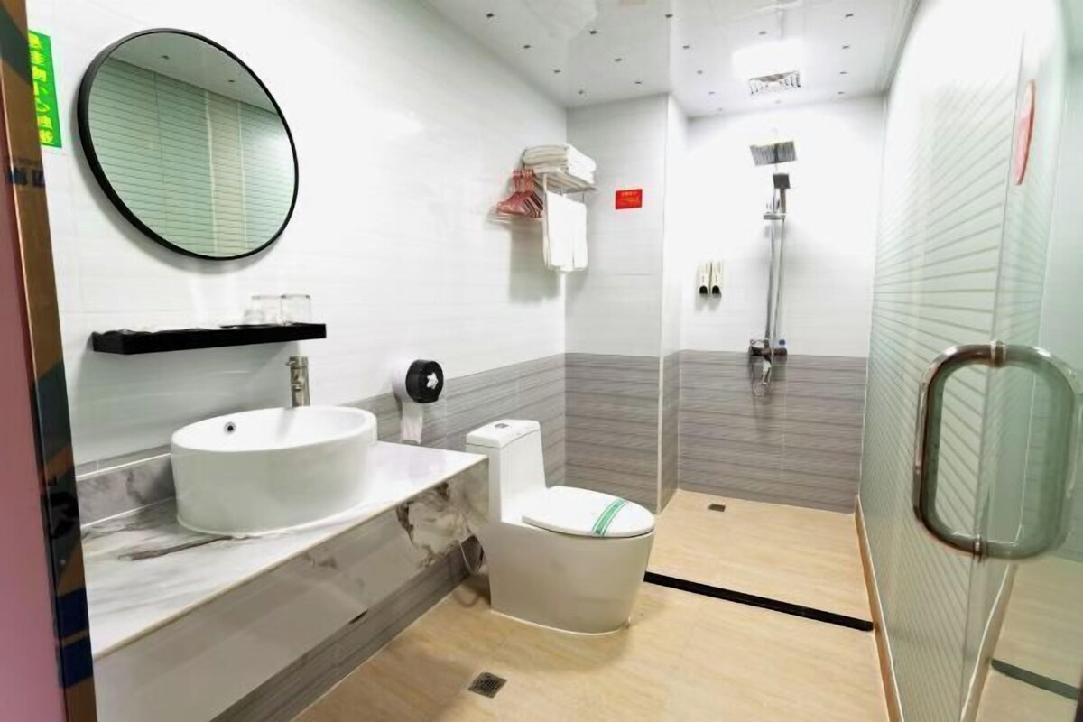 Un bany modern amb un mirall rodó, un lavabo, un vàter i una zona de dutxa.