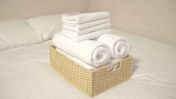A neatly folded stack of white towels in a wicker basket on a bed with white bedding.