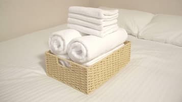 A stack of white towels in a woven basket on a bed with white linens.