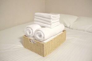 Een stapel witte handdoeken in een gevlochten mand op een bed met witte lakens.