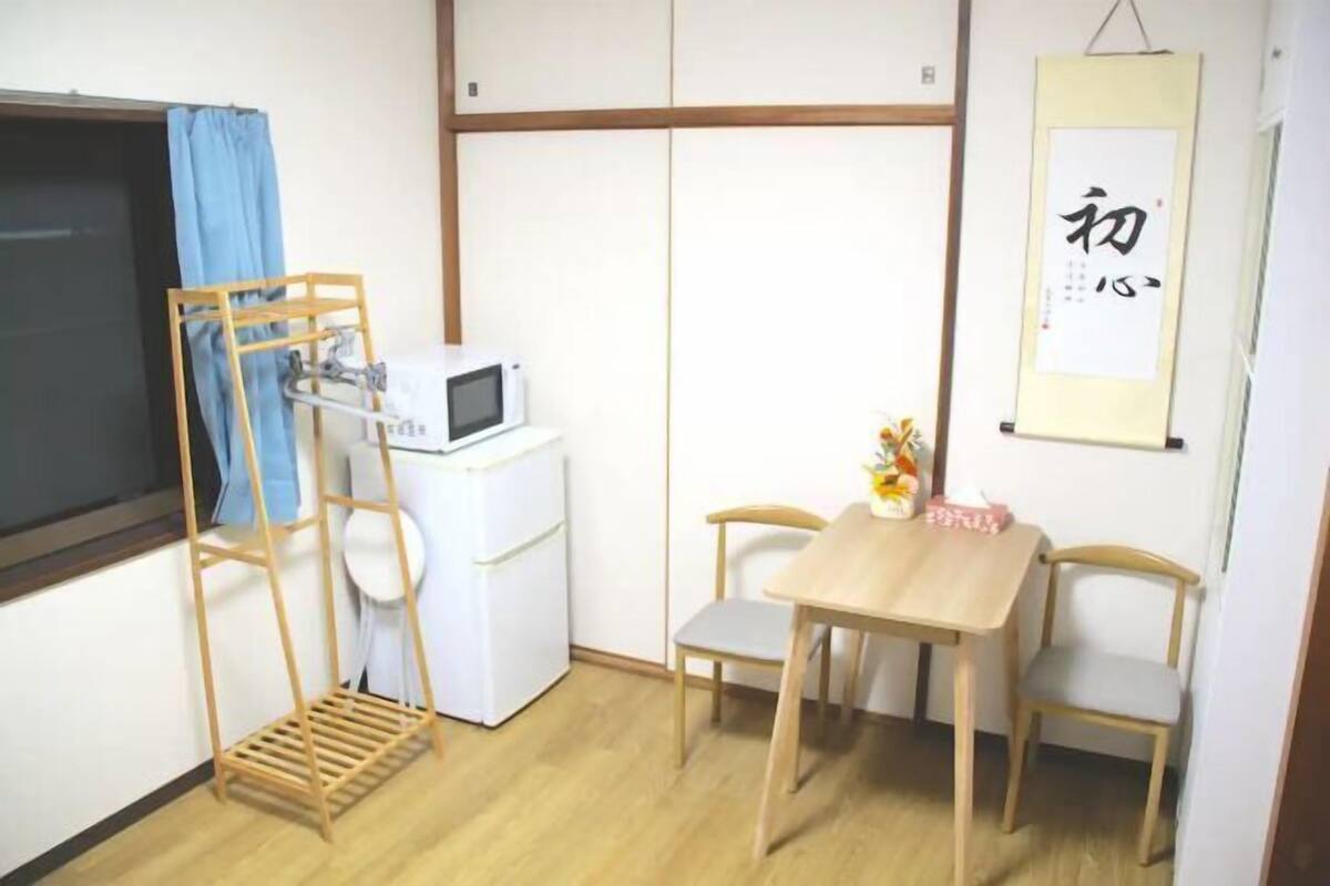 Une petite pièce, de taille modeste, avec une table en bois et deux chaises, un réfrigérateur blanc, un four à micro-ondes et un rideau bleu.