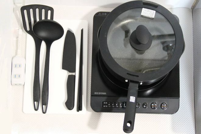 A kitchen with a black induction cooktop, a black pot with a lid, a spatula, a knife, and a pair of tongs.