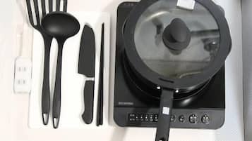 A kitchen with a black induction cooktop, a black pot with a lid, a spatula, a knife, and a pair of tongs.