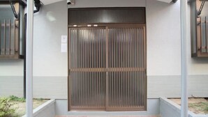 A gated entrance with a metal sliding door, a brick pathway, and a white wall with a small sign. - Kokoro no sato・Ren (Kyoto)