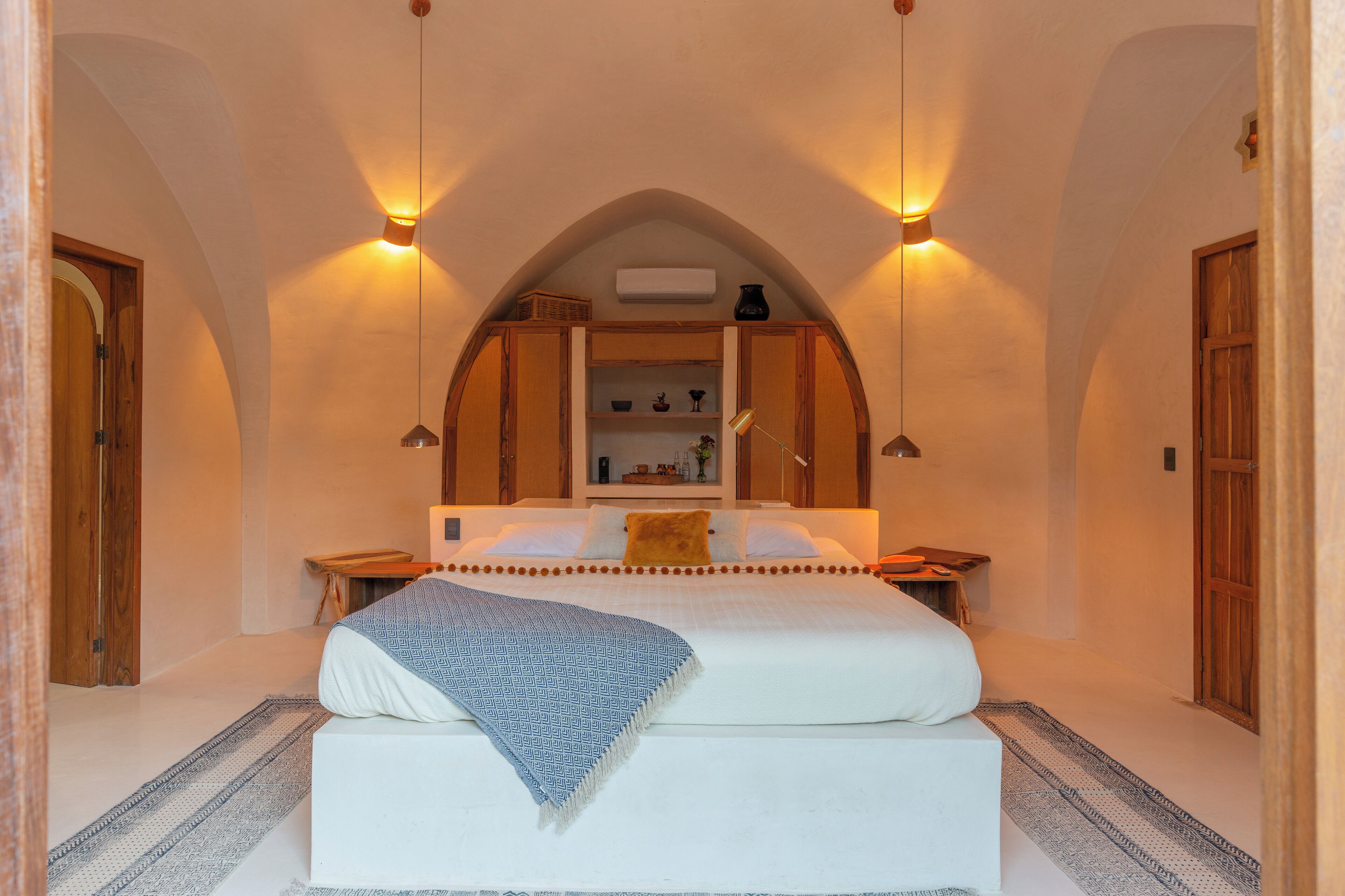 Een slaapkamer met een groot bed, een houten hoofdbord, een inbouwkast met decoratieve items en twee wandlampen.