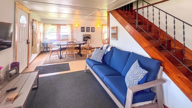Un espacio acogedor con un sofá azul, una escalera de madera y una mesa de comedor con sillas.
