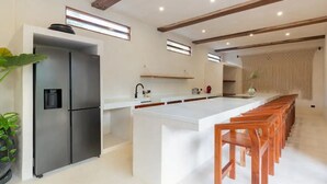 A modern kitchen with a central island, stainless steel appliances, and wooden chairs. - Villa Sanah 11 con alberca privada ubicada en Tulum (Tulum)