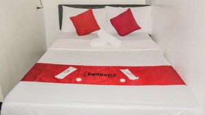 Uma cama bem arrumada com lençóis brancos, duas almofadas vermelhas, uma toalha branca e um cobre-leito vermelho com um logotipo.