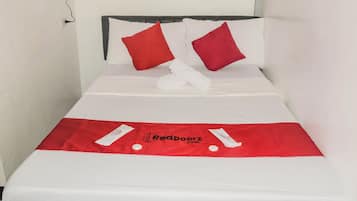 A neatly made bed with white linens and two red pillows, a white towel, and a red bedspread with a logo.