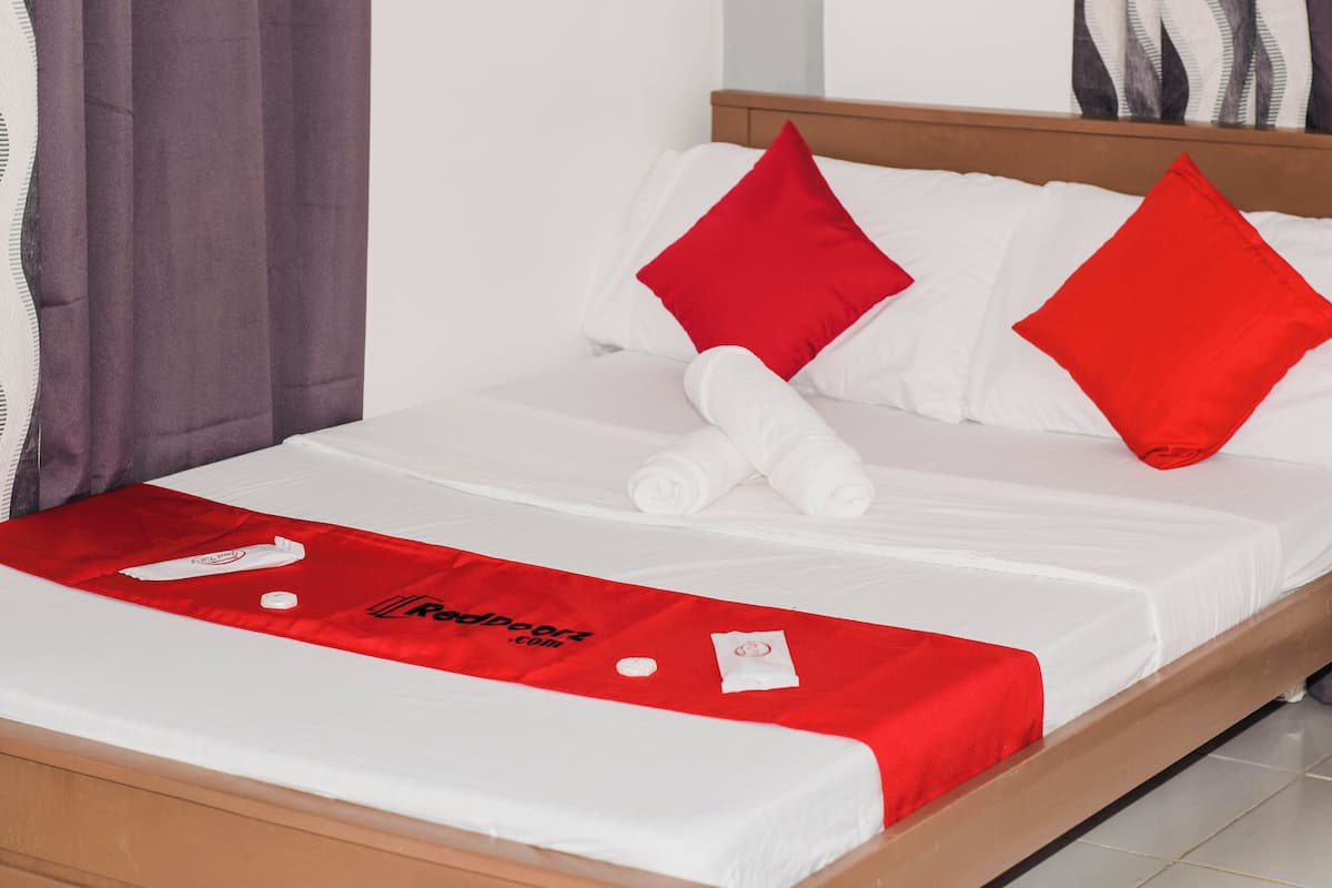 A neatly made bed with white sheets and red pillows, a red towel on the bed, and a red blanket with a logo.