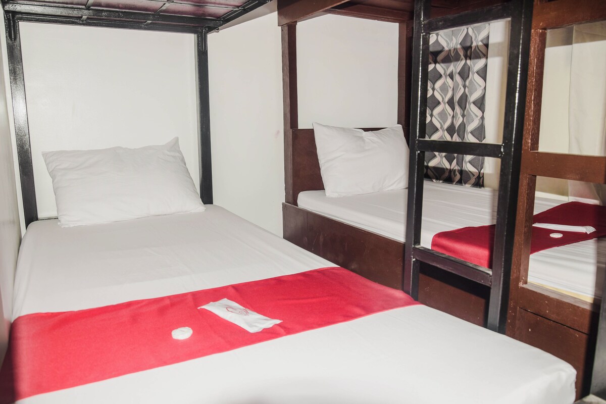 A room with two beds, each with white bedding and a red accent.
