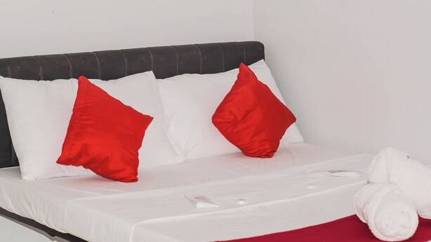 A neatly made bed with white and red pillows, a white blanket, and a rolled white towel. - Reddoorz @ Gabz K Travellers Inn Sorsogon City (Sorsogon City)
