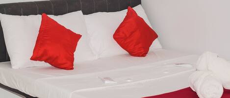 Una cama bien hecha con almohadas blancas y rojas, una manta blanca y una toalla blanca enrollada.