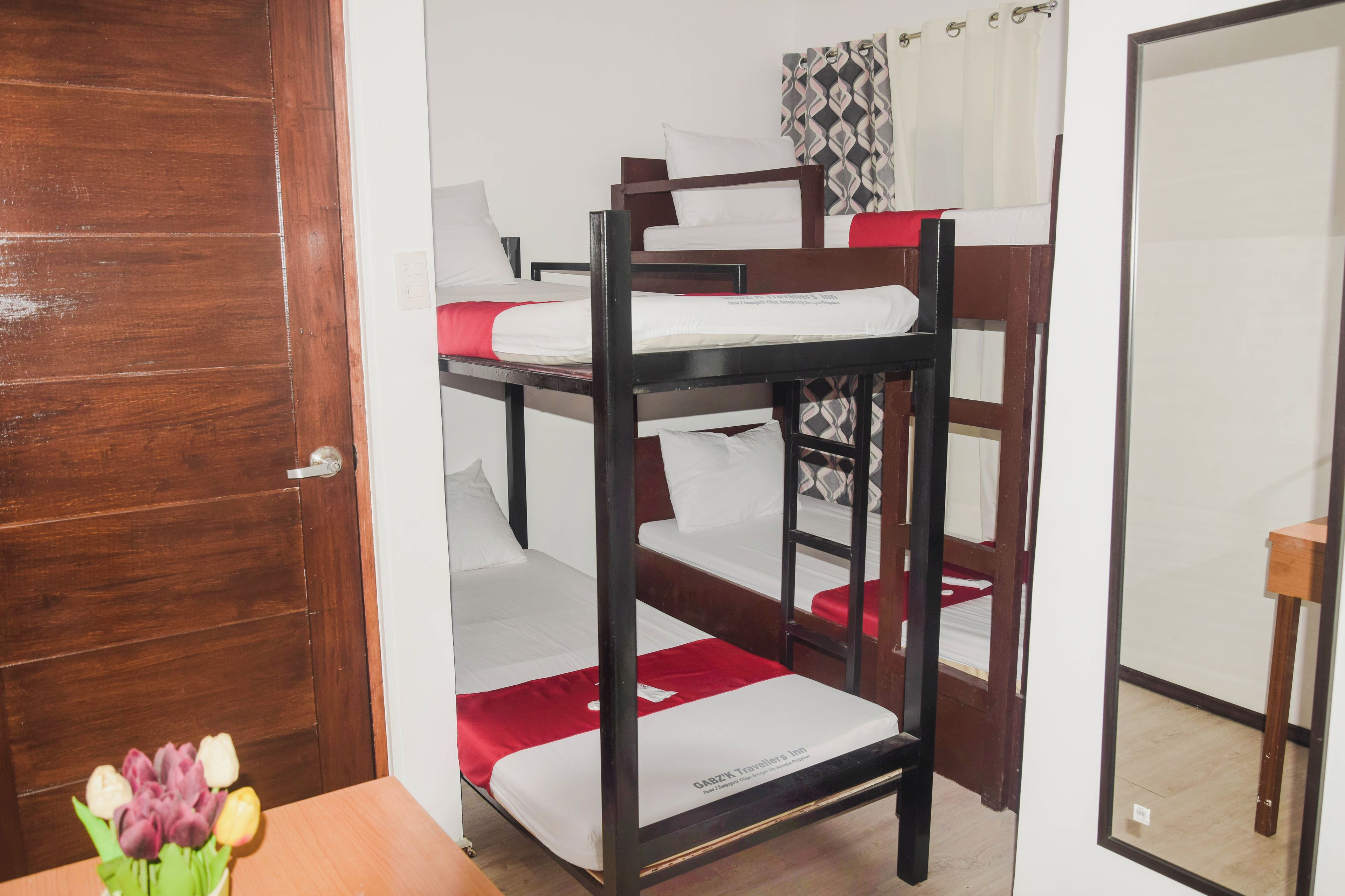 A bunk bed room with a wooden door, a small table with a vase of flowers, and a mirror on the wall.