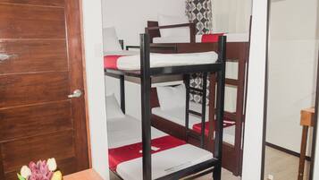 A bunk bed room with a wooden door, a small table with a vase of flowers, and a mirror on the wall.