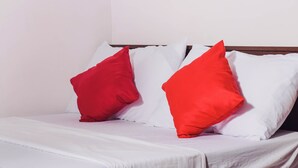 Uma cama com roupa de cama branca e duas almofadas vermelhas.