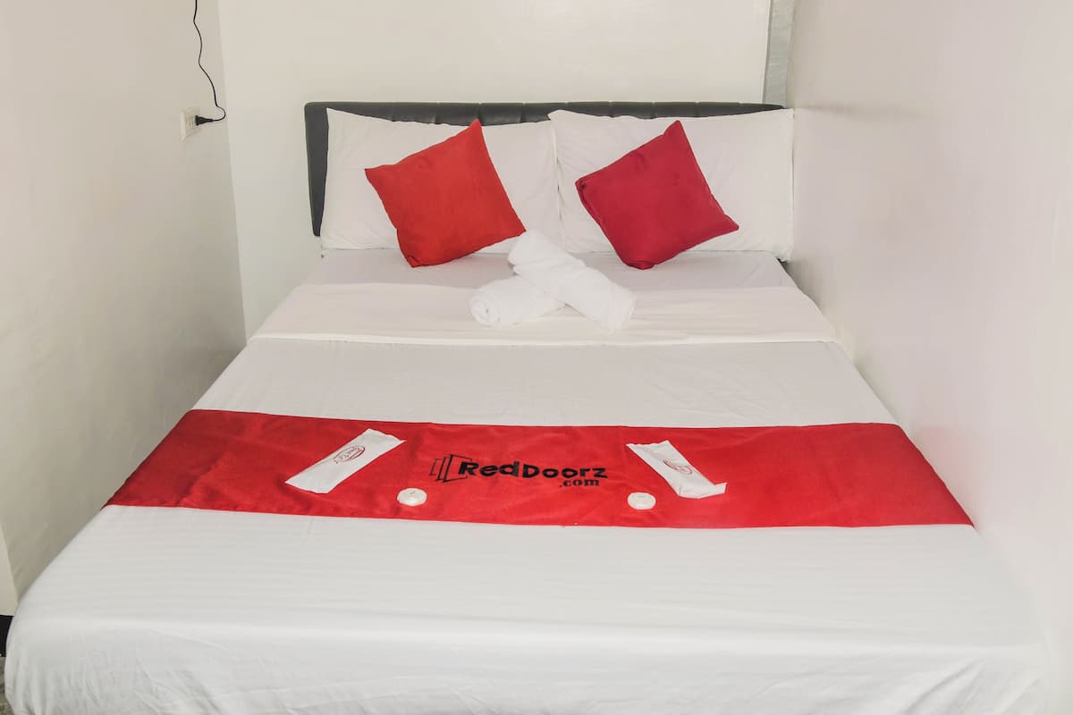 A neatly made bed with white linens and two red pillows, a white towel, and a red bedspread with a logo.