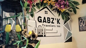 A wall with a 'GABZ'K Travellers Inn' sign, surrounded by decorative plants and a rustic sculpture. - Reddoorz @ Gabz K Travellers Inn Sorsogon City (Sorsogon City)