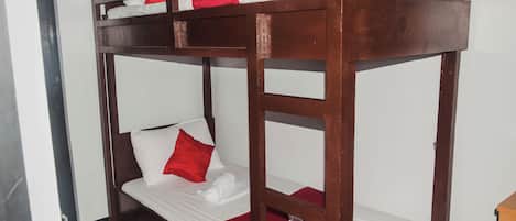 Una cama individual con ropa blanca y detalles rojos, un armazón de madera y una mesita de madera al lado.