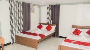A hotel room with two beds, each with a wooden frame and white bedding. There are red pillows and a red blanket on one bed, and a red towel on the other. The room has a tiled floor and curtains with a wavy pattern. - Reddoorz @ Gabz K Travellers Inn Sorsogon City (Sorsogon City)