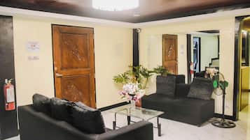 A lobby with a reception desk, a black sofa, a glass coffee table, and a potted plant.