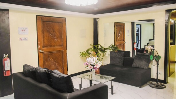 Um hall de entrada com balcão de recepção, um sofá preto, uma mesa de centro de vidro e uma planta em vaso.