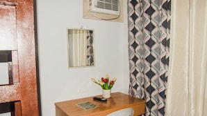 A small room with a wooden desk, a chair, a mirror, a wall-mounted air conditioner, and a patterned curtain. - Reddoorz @ Gabz K Travellers Inn Sorsogon City (Sorsogon City)